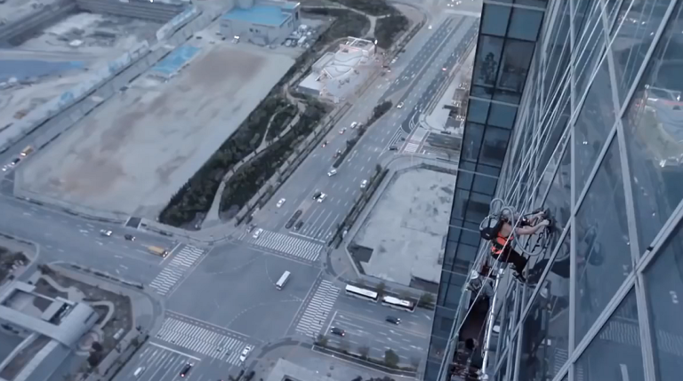 Une femme tente d’escalader un immeuble avec deux aspirateurs