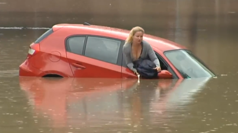 Une femme sur le toit de sa voiture dans une inondation