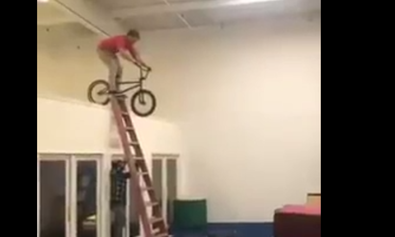 Un jeune tente sauter sur un matelas en vélo en étant sur une échelle