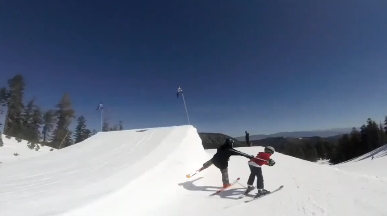 Un skieur pousse un enfant qui passe devant lui sur un tremplin