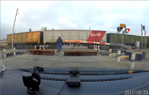 Un cycliste passe entre deux trains à un passage à niveau en mode « Je suis seul dans la vie »