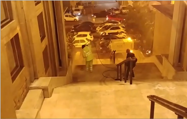 Un employé de la Mairie de Marseille arrose un vieil homme assis sur des escaliers