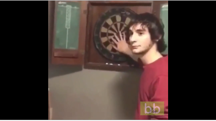 Il tire une fléchette alors que son pote a sa main sur la cible.