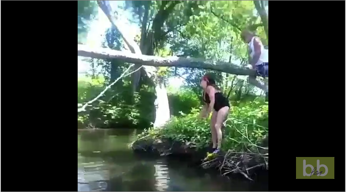 Une femme saute sur un arbre pour se suspendre au dessus d’une rivière
