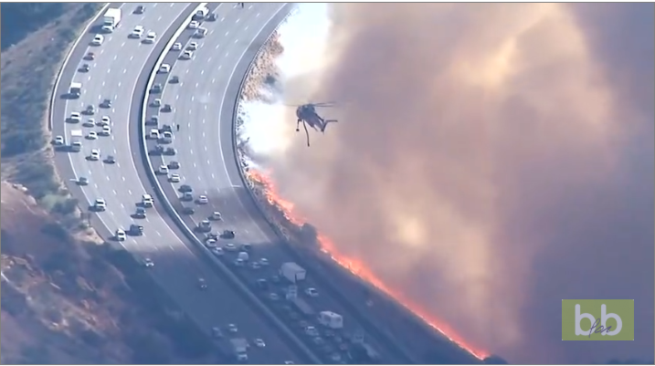 Un hélicoptère largue de l’eau sur une autoroute qui se fait attaquer par les flammes en Californie