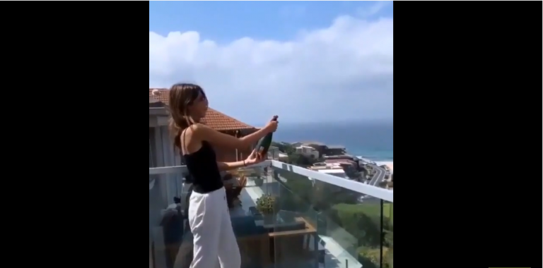 Une blonde veut ouvrir une bouteille de champagne depuis son balcon