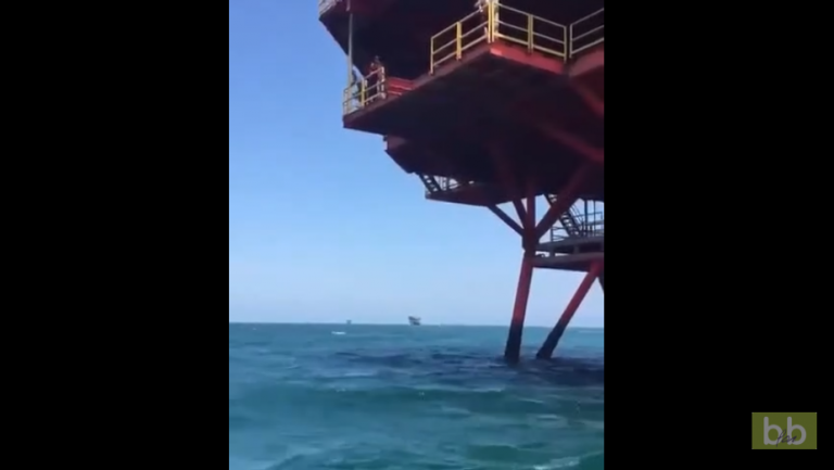 Une fille hésite avant de sauter dans la mer depuis une plateforme pétrolière