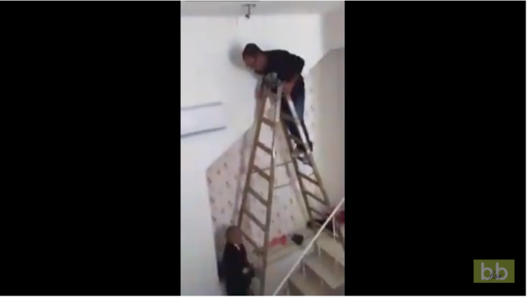 Un homme essaye d’accrocher un lustre en haut des escaliers